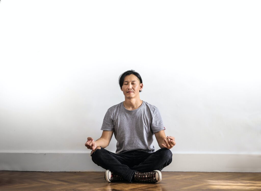 A man displaying a positive state of mental health by sitting with his eyes closed in the meditation position
